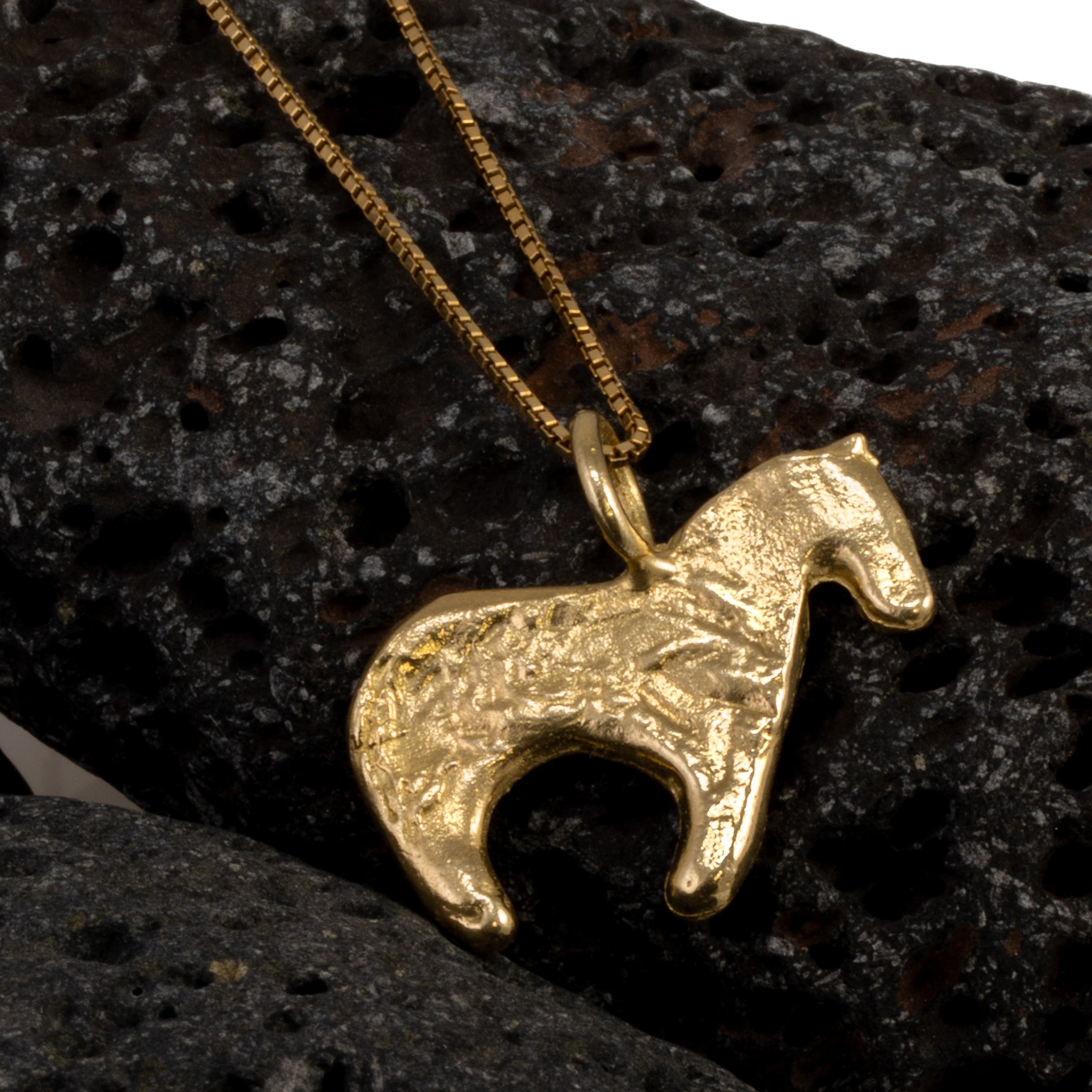 Firehorse Pendant in bronze with chain on dark volcanic rock, dramatic close-up — Zefiro Jewels